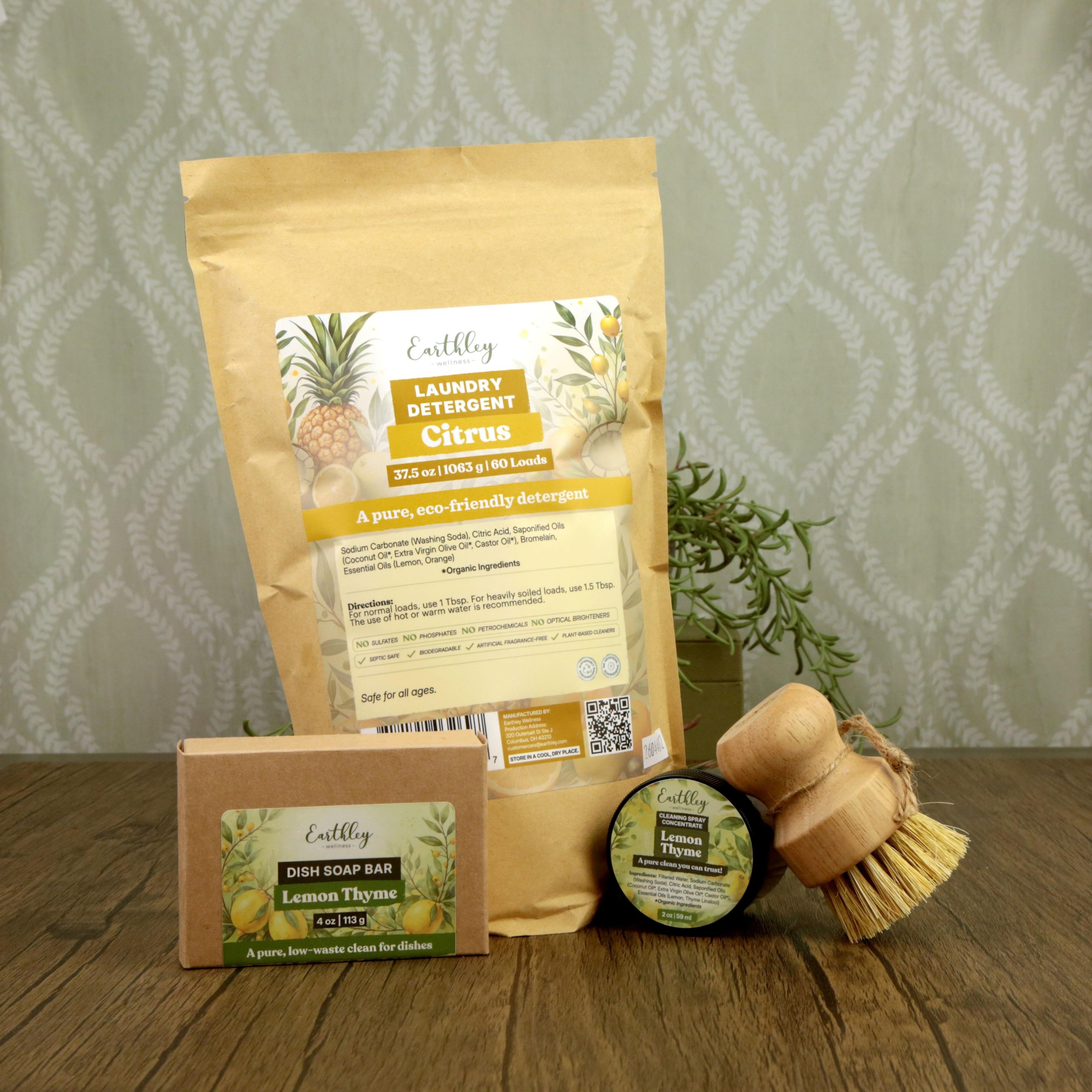 Earthley citrus laundry detergent pouch, lemon thyme dish soap bar and cleaning scrub with wooden brush on wood surface