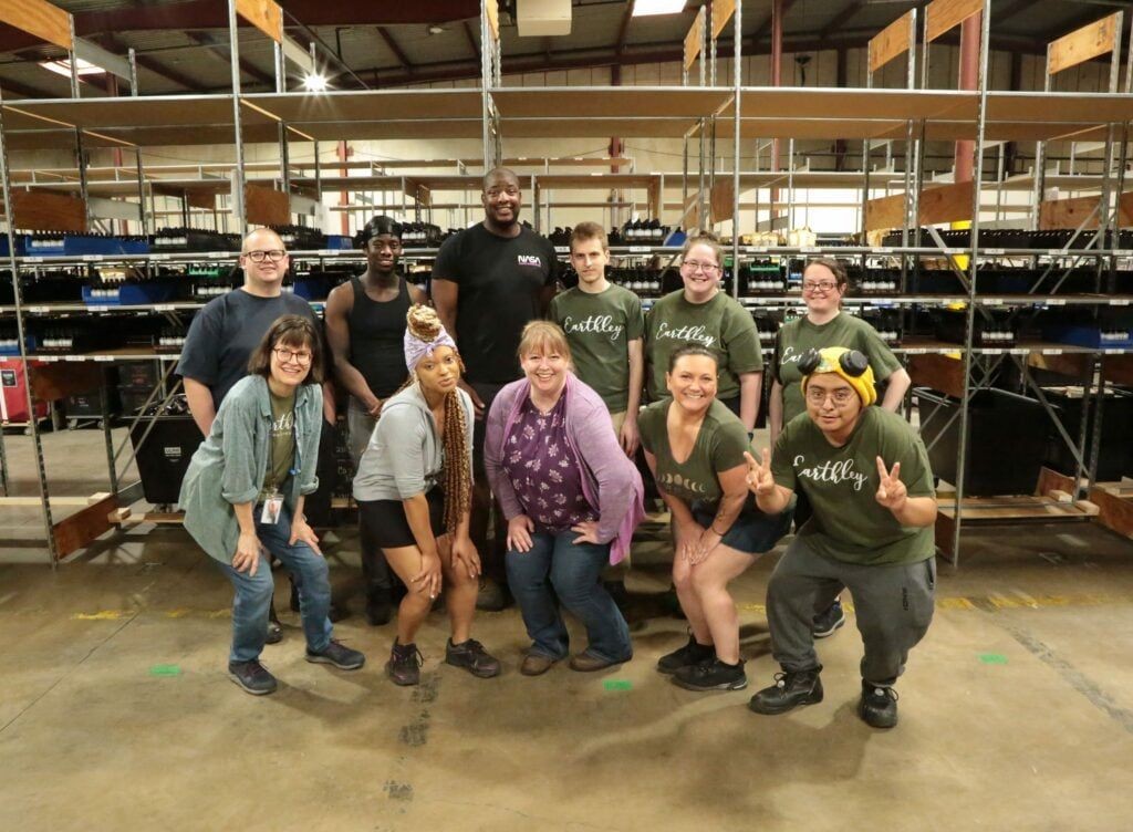 Earthley Yearbook 2023 Shipping Team group photo showing employees in casual attire in warehouse setting with brown shipping boxes and gray shelving
