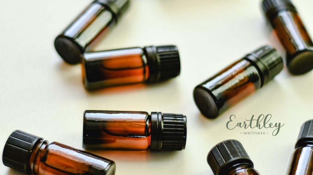 Amber glass essential oil bottles with black caps scattered on cream background with Earthley wellness logo