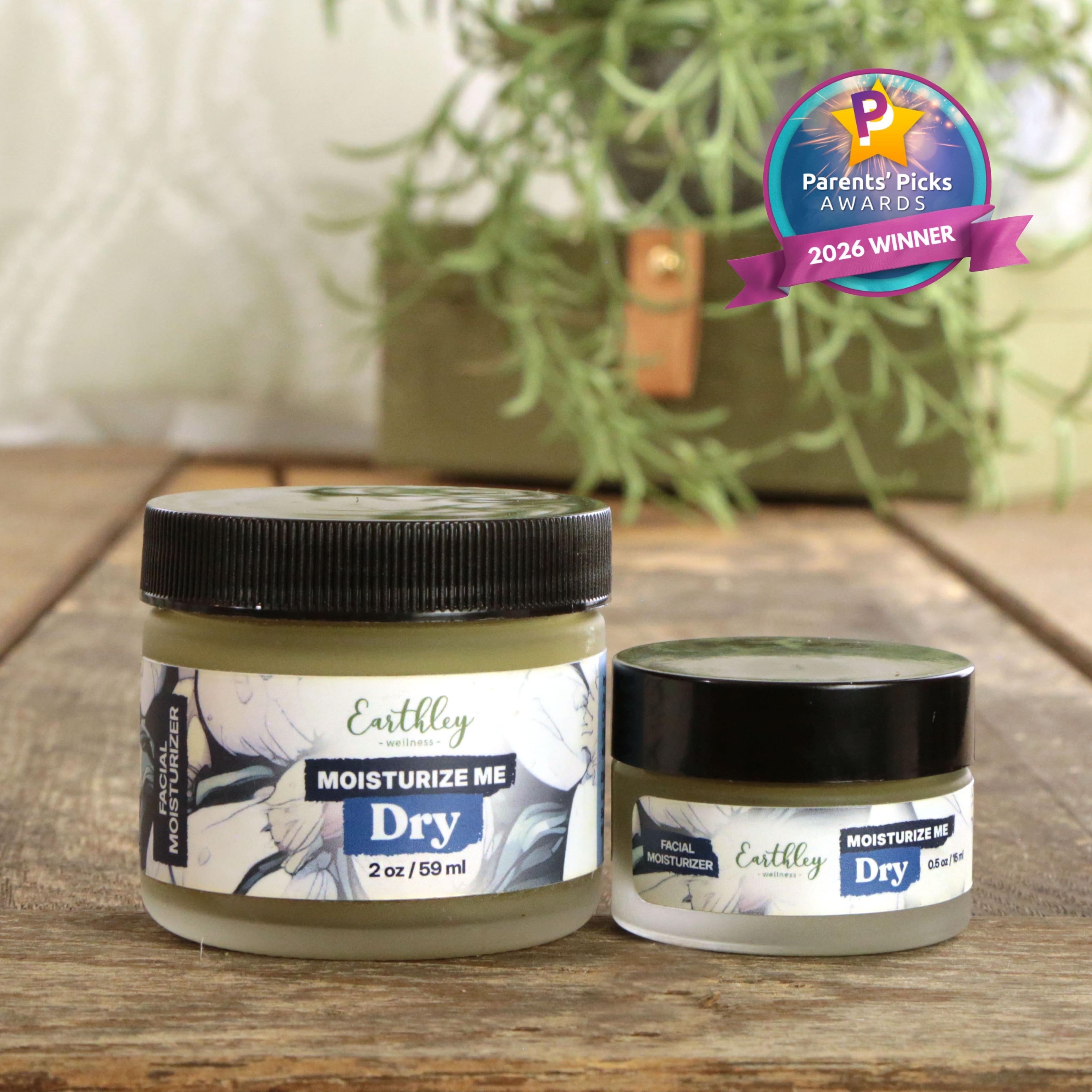 Two jars of Earthley Moisturize Me Dry facial moisturizer on wooden surface with plants, featuring Parents' Picks 2026 Winner award badge