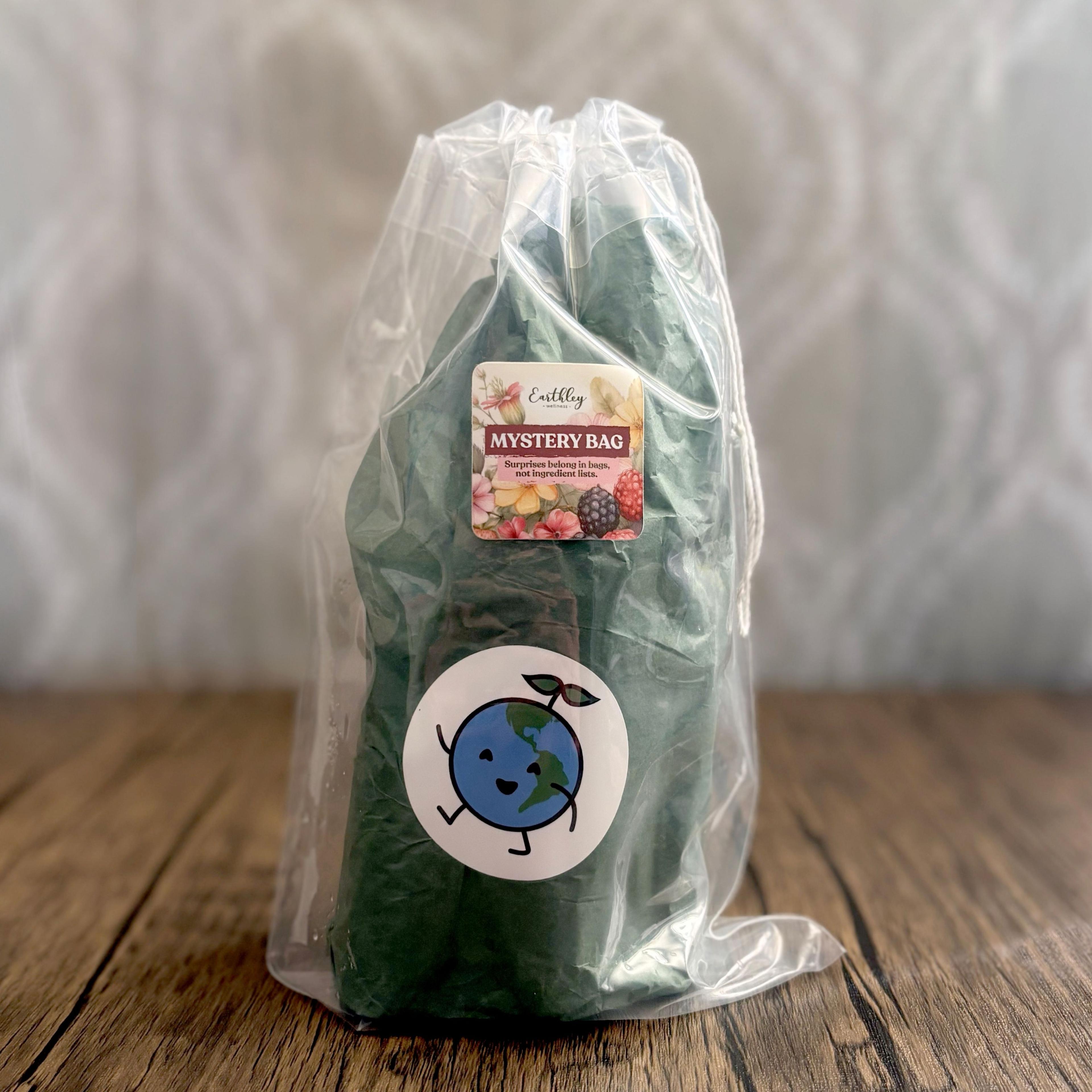 Earthley Wellness mystery bag in clear plastic wrap with green tissue paper and Earth-themed sticker on wooden surface