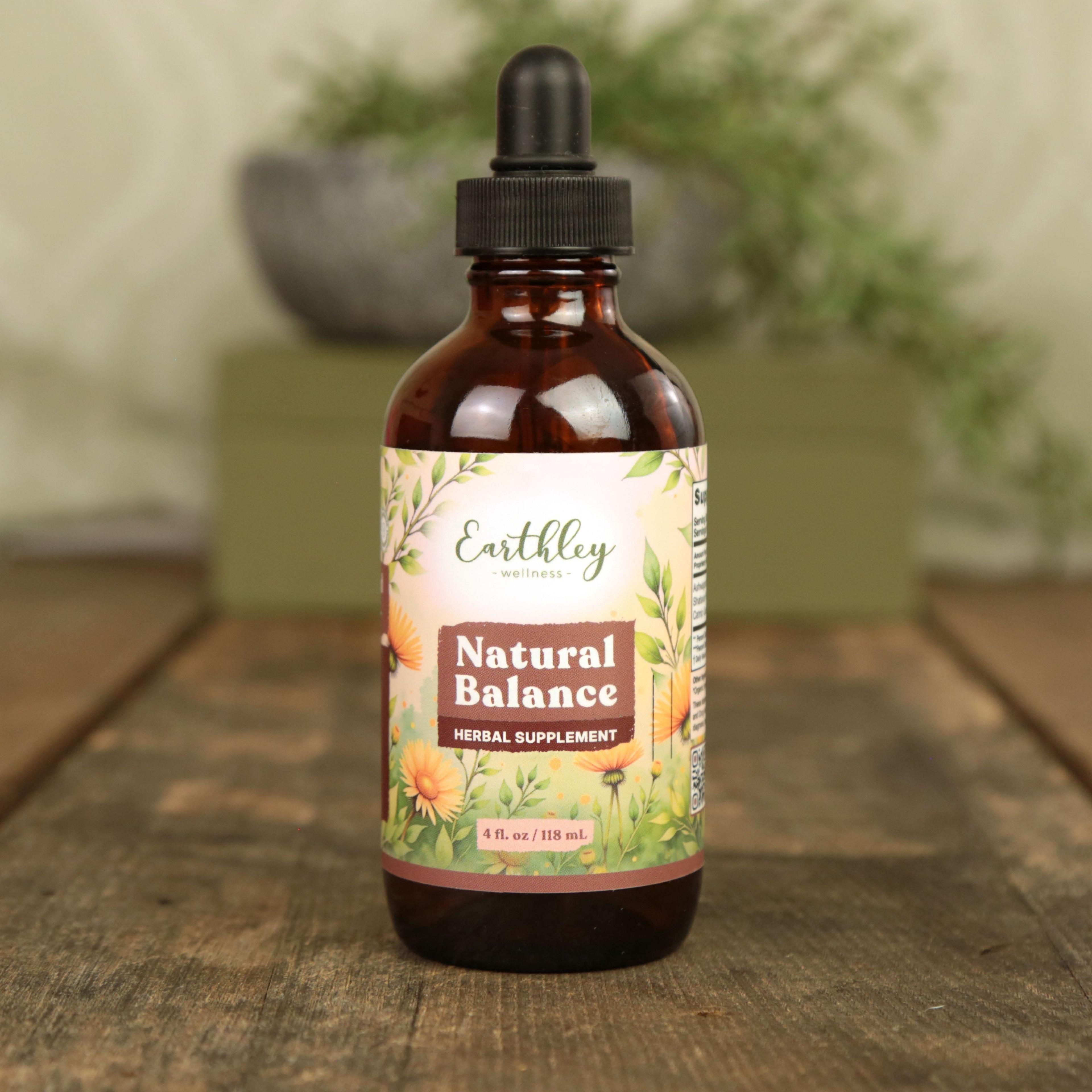 Earthley Natural Balance 4 fl oz amber dropper bottle with orange calendula flower and green botanical leaf label on rustic wood surface with potted fern plant in background