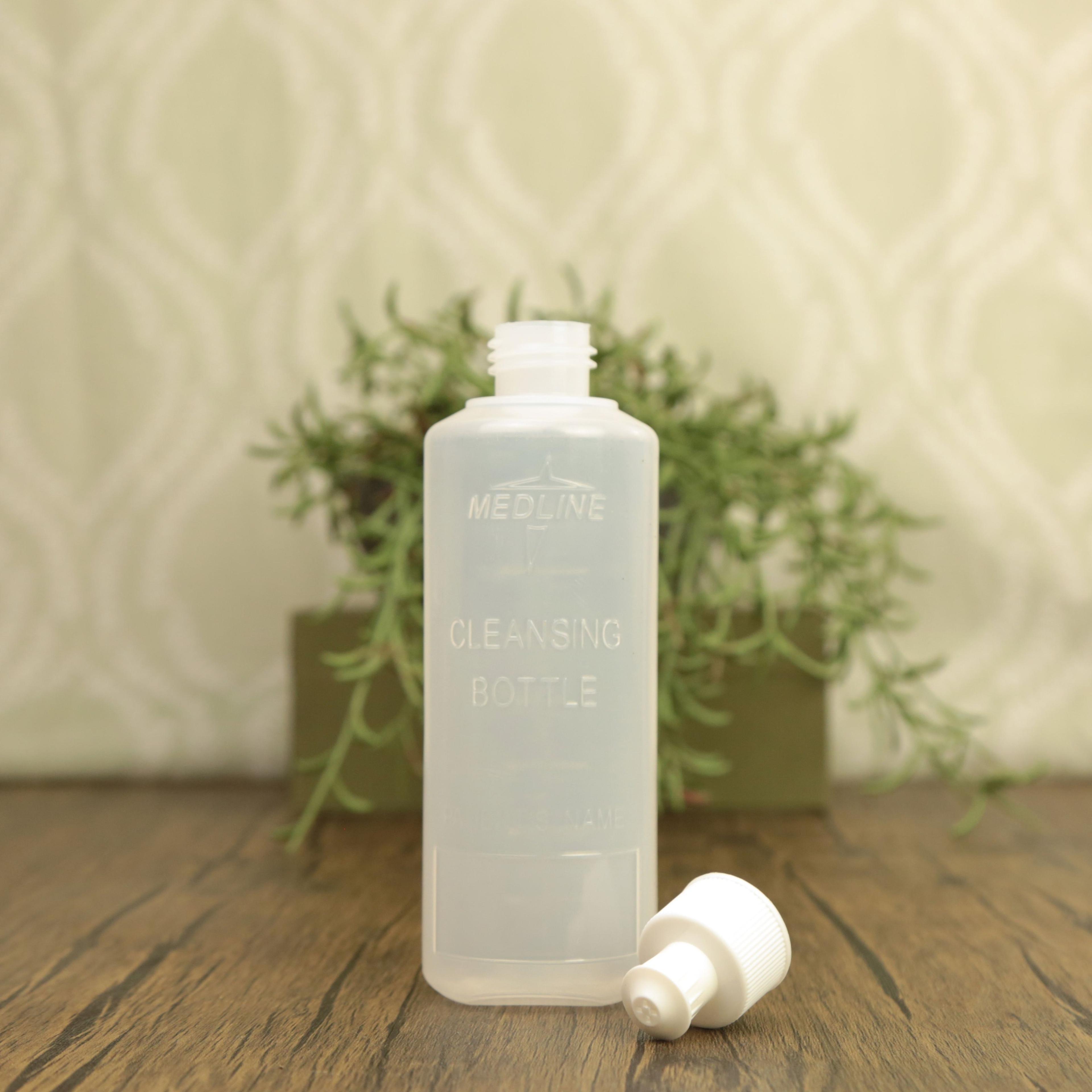 Clear plastic bottle labeled "Medicine Cleansing Bottle" with white cap beside it on wooden surface with green plant background
