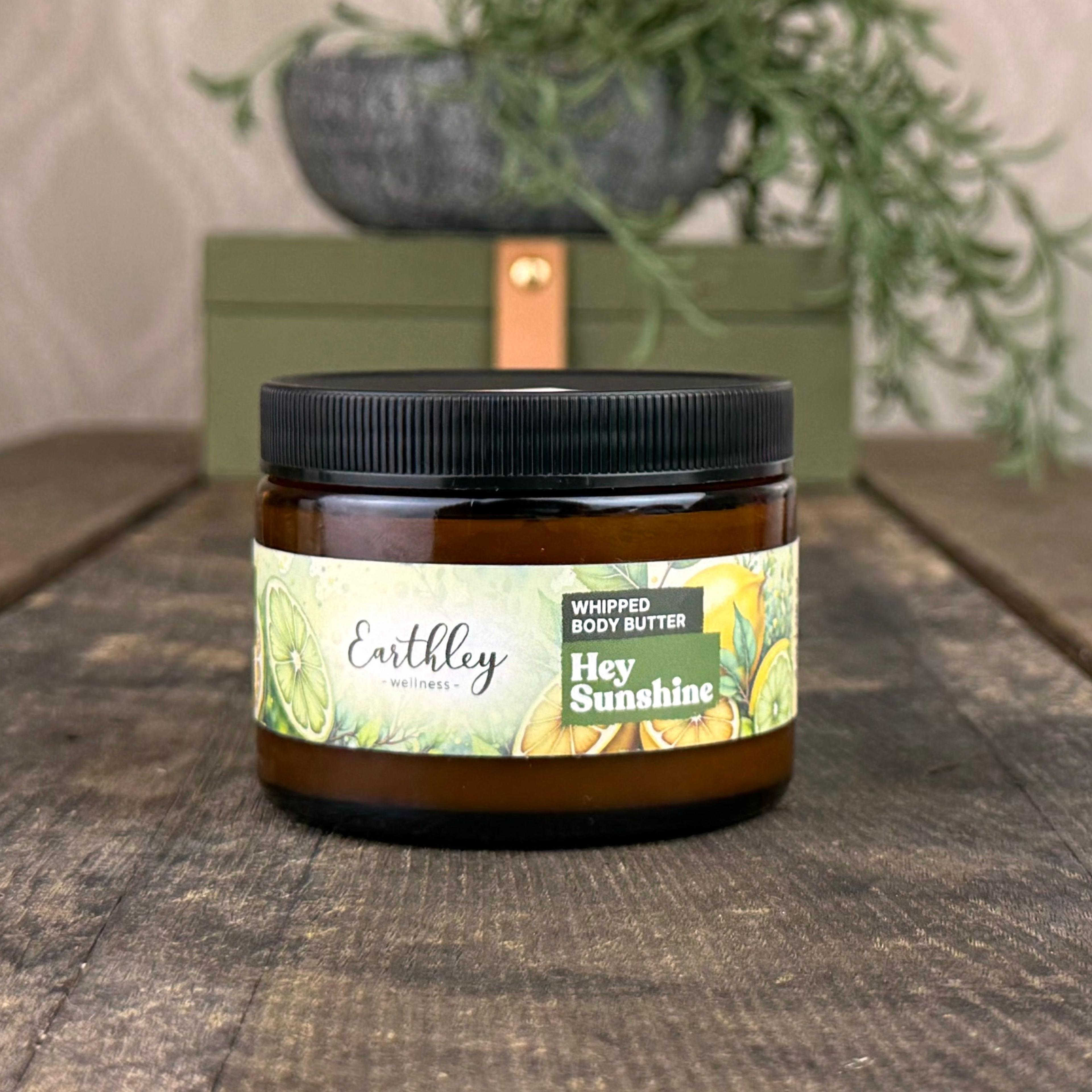 Earthley Hey Sunshine whipped body butter jar with citrus botanical label on wooden surface with plants