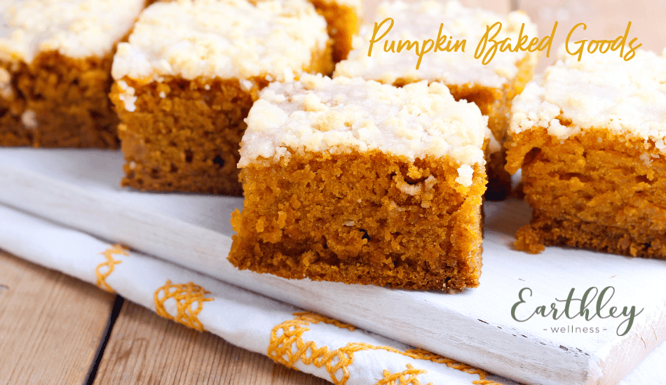 Pumpkin Baked Goods recipe header showing orange pumpkin cake bars topped with cream cheese frosting on white parchment paper with gold and white striped napkin on wooden surface