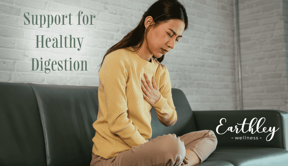Support for Healthy Digestion blog header showing woman in mustard yellow sweater sitting on gray couch holding stomach and chest with uncomfortable expression