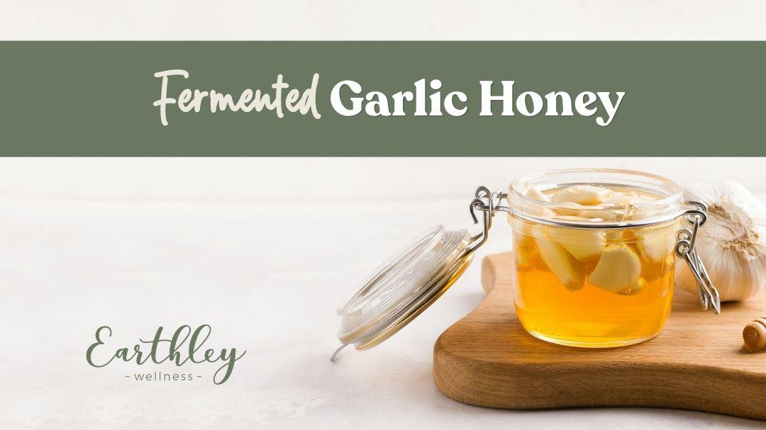 Garlic cloves submerged in golden honey inside an open glass jar on a wooden cutting board.
