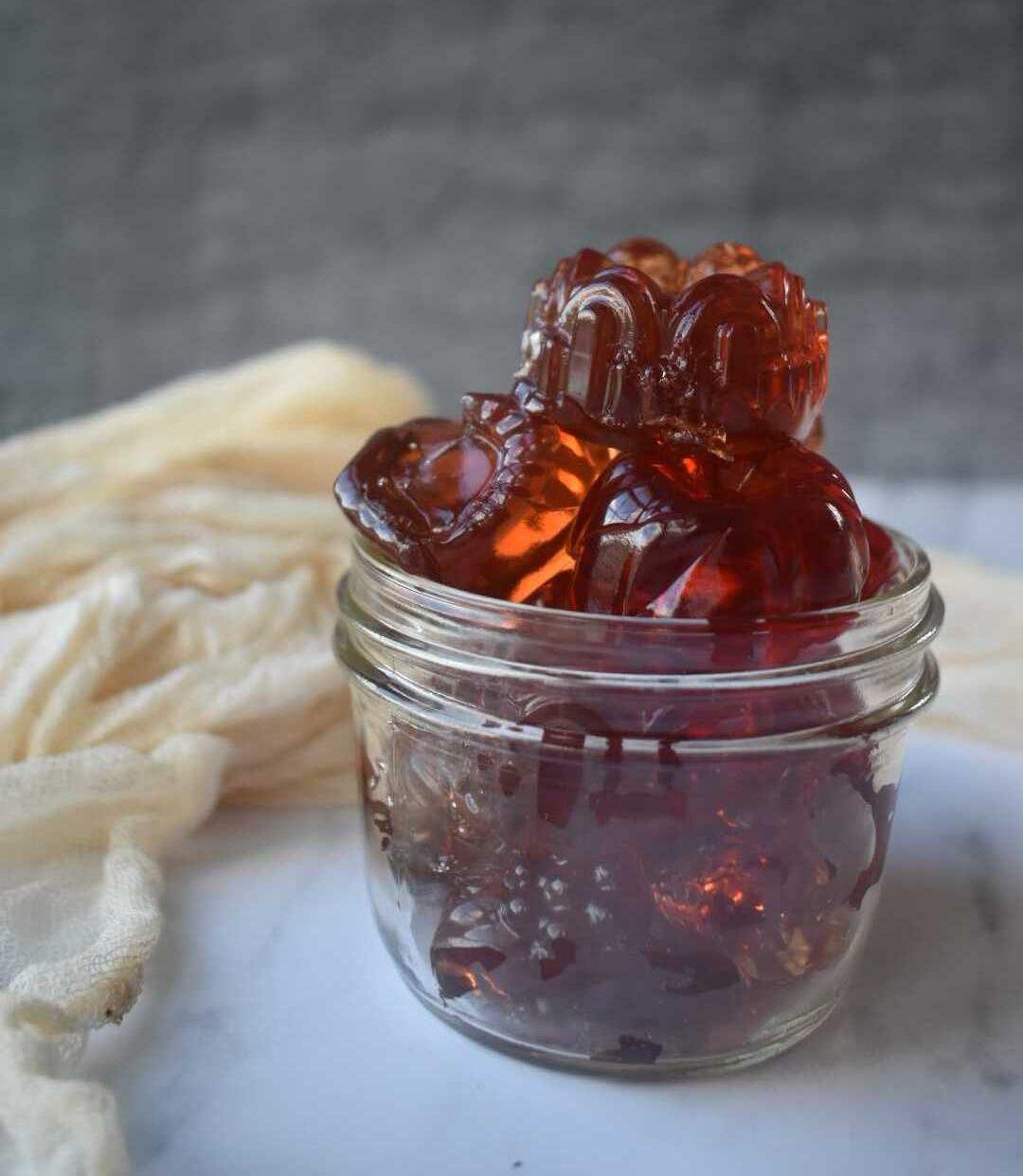 Dark amber herbal gummies in glass jar with cream cloth on marble surface