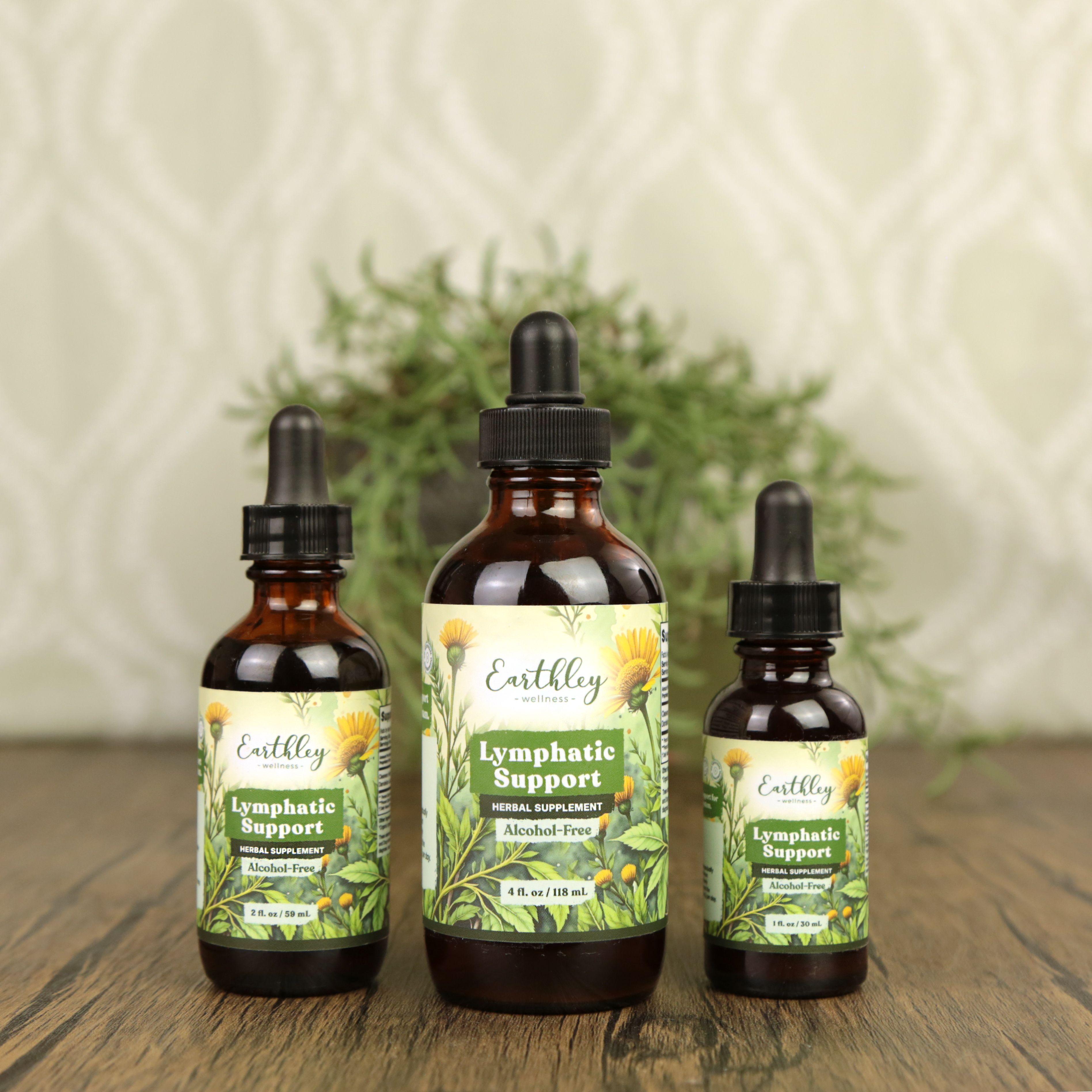 Three Earthley Lymphatic Support amber dropper bottles in 1 oz, 2 oz, and 4 oz sizes with green botanical labels featuring dandelions showing Alcohol-Free designation arranged on wooden surface with greenery in background