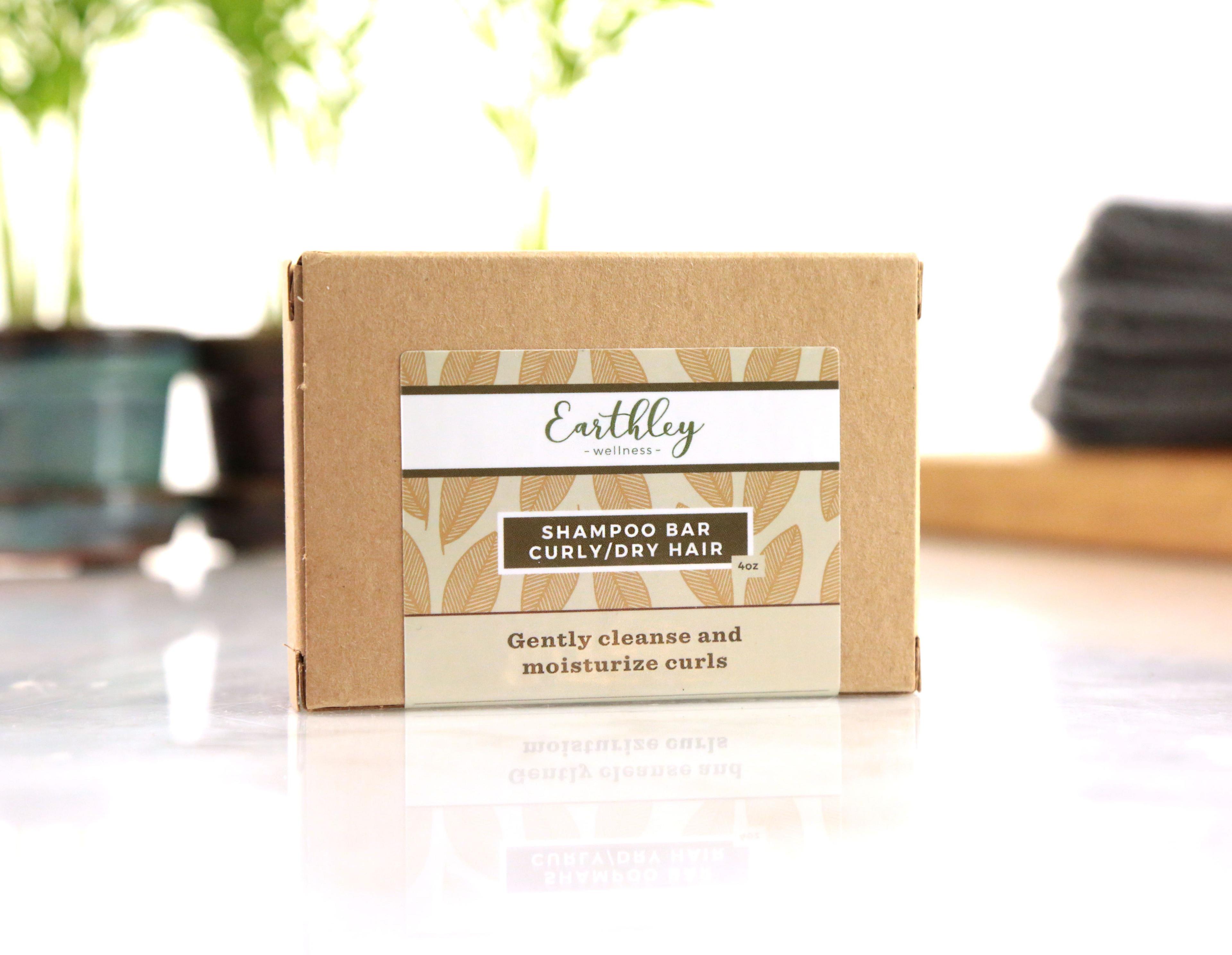Earthley Shampoo Bar for Curly/Dry Hair in kraft paper box with leaf pattern label on reflective surface with plants in background
