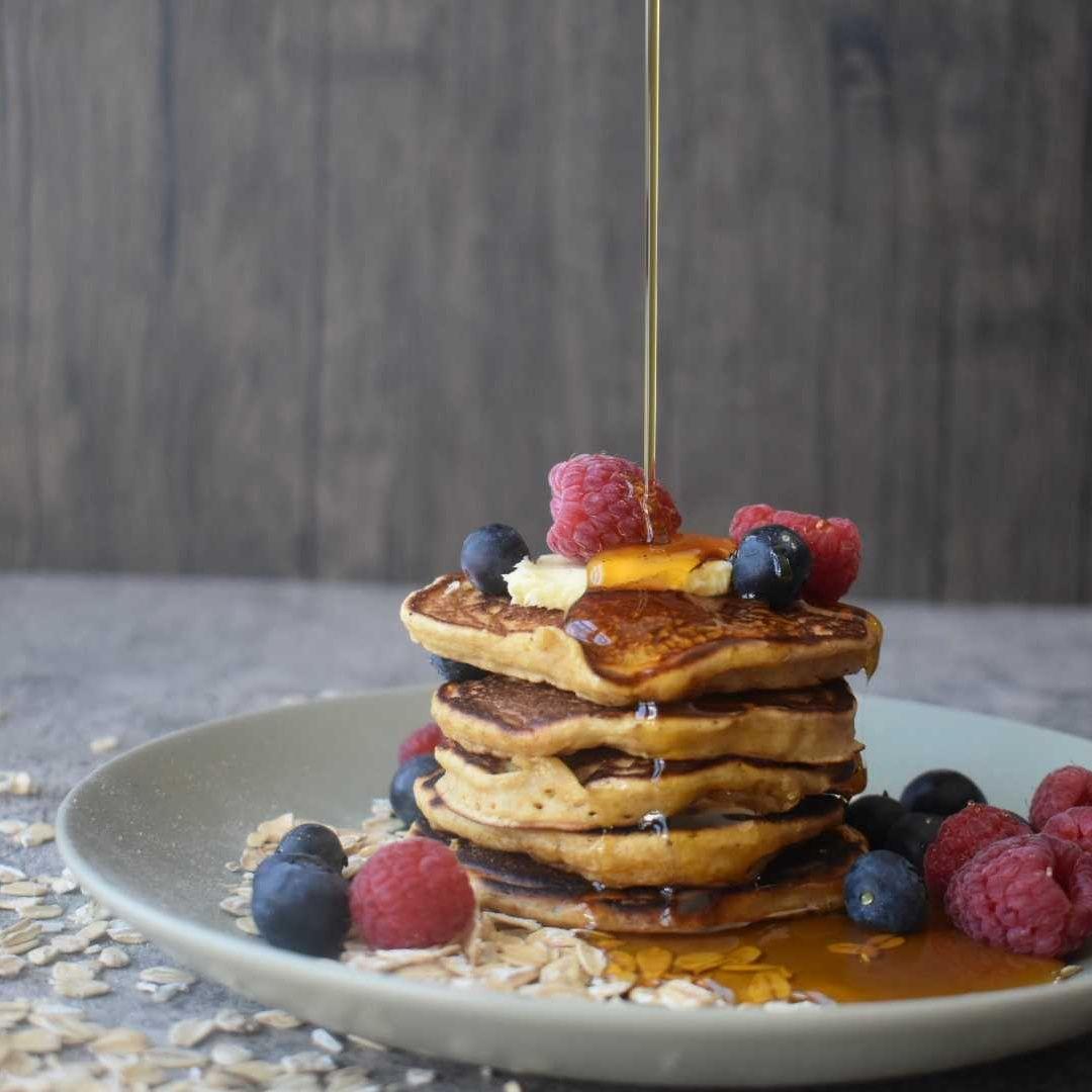 Stack of golden pancakes topped with fresh berries and honey drizzle on white plate