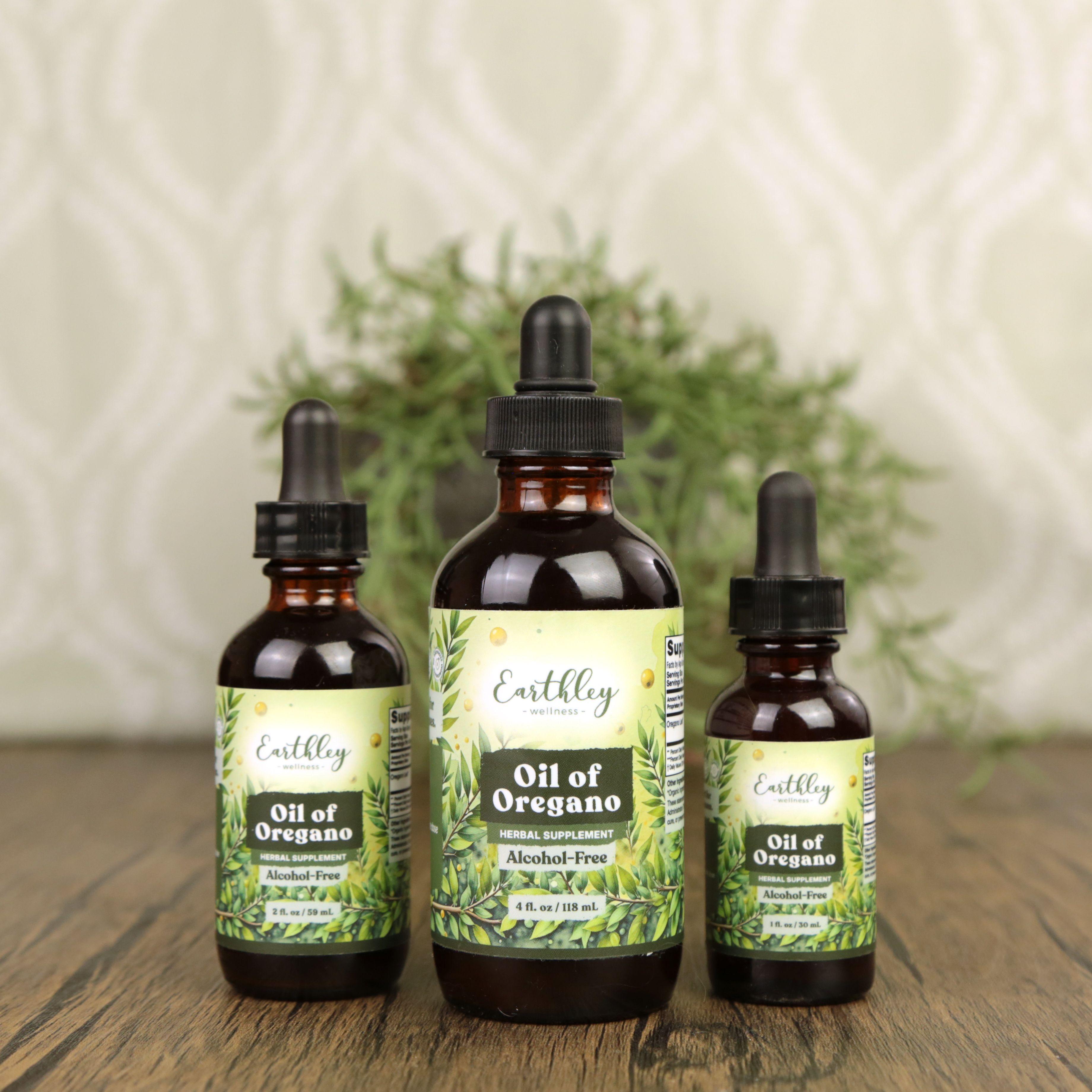 Three Earthley Oil of Oregano amber dropper bottles in 1 oz, 2 oz, and 4 oz sizes with green oregano leaf labels showing Alcohol-Free designation arranged on wooden surface with rosemary plant in background