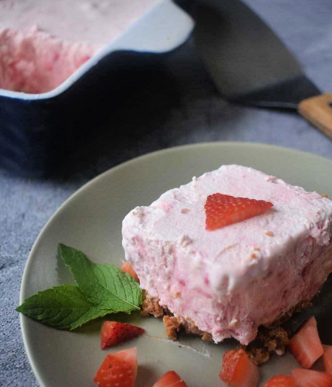 Pink strawberry cheesecake slice on white plate with fresh strawberries and mint garnish