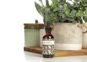Earthley Vaccine Detox 2oz amber glass dropper bottle with black cap and sage green olive leaf pattern label on wooden cutting board with green plants in cream and white ceramic pots with sage green ribbed canister
