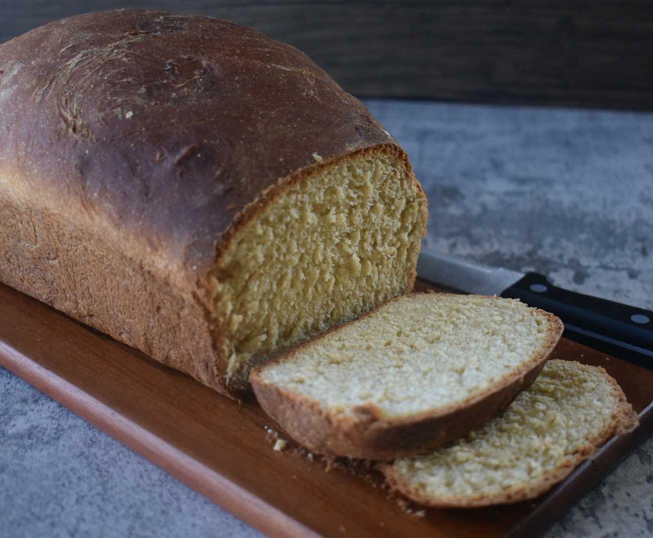Freshly baked whole grain bread loaf partially sliced on wooden cutting board with knife